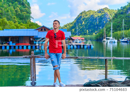 Young man posing on pier at floating fish farm in Asia 75104683