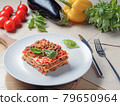 Piece of lasagna on white plate. Basil, tomatoes 79650964