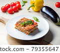 Piece of lasagna on white plate with vegetables 79355647