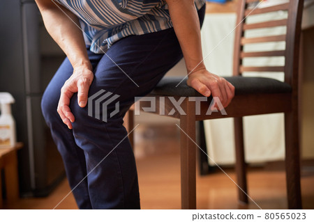 Senior woman standing up from a chair while avoiding knee pain 80565023