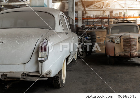 Many rusty abandoned forgotten antique oldtimer old car and motorcycles at junkyard factory storage warehouse indoors. Classic vintage retro vehicle detail garage workshop restore renovation station 80966583