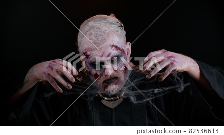 Sinister man with horrible scary Halloween dead zombie makeup in costume looking ominous at camera 82536613