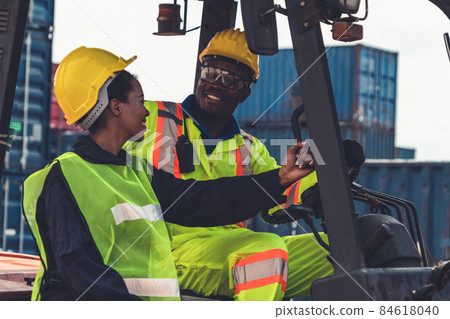 African american man and woman driving forklift in shipyard . 84618040