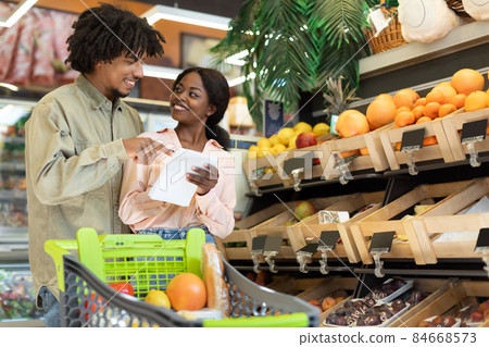 Cheerful Black Couple With Shopping List Buying Groceries In Store 84668573