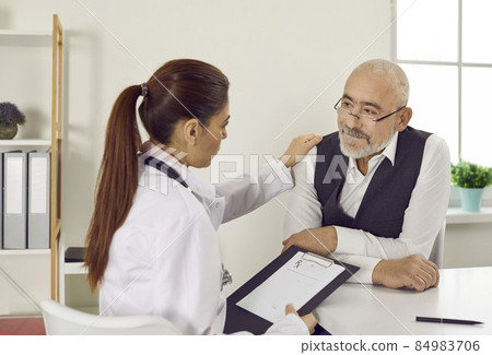 Caring young woman doctor comfort support mature male patient at consultation in clinic. Attentive female nurse touch shoulder caress senior man in hospital. Good medical service. Health insurance. 84983706