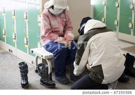 Parents and children in masks preparing for snowboarding in front of a coin locker at a ski resort 87193366