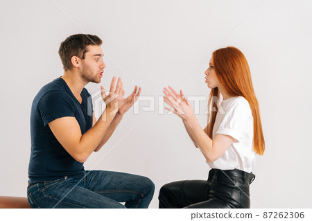 Studio shot of displeased young couple quarreling, actively gesturing with hands, talking and shouting at each other on white isolated background. Concept of relationship crisis. 87262306