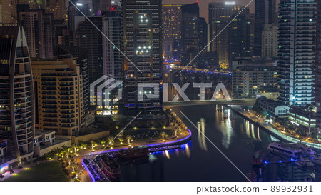 Dubai Marina with several boats and yachts parked in harbor and skyscrapers around canal aerial night to day timelapse. 89932931