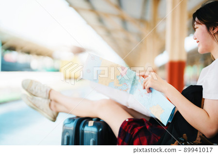 summer, relax, vacation, travel, portrait of a cute Asian girl looking at a map to plan a trip while waiting at the train station 89941017