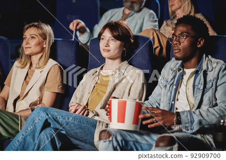 Group of ethnically diverse people sitting in modern cinema with blue chairs watching movie 92909700