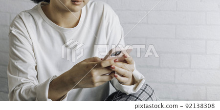 girl is texting on a smartphone while sitting on a bed at home. copy space. teenage girl with problematic skin, with a therapeutic cream applied. 92138308