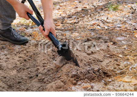 Man digs soil with a shovel in the forest. Black shovel in human hands. Sunny. 93664244