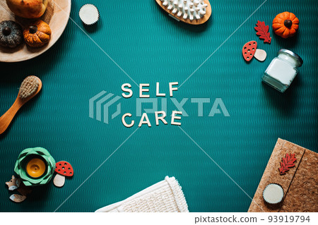 Self-care word on green background flat lay. Self-care text wooden letters with body face care products and autumn decor 93919794