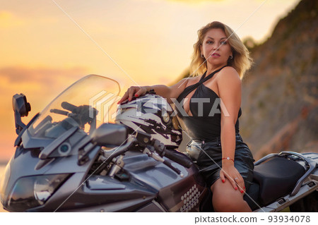 World motorcyclist day. Portrait of beautiful caucasian adult blonde woman confidently poses by a motorcycle with moto helmet. The concept of motorbike travel 93934078