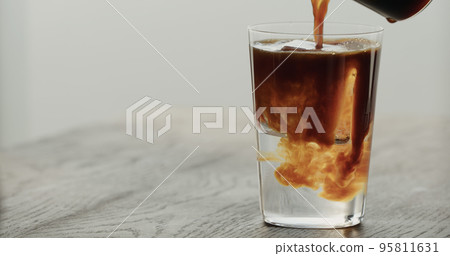 man pour espresso into tonic with clear ice cube in tumbler glass on black oak table 95811631