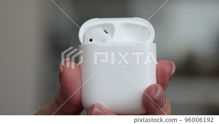 Woman hands putting back the wireless earbuds in the charging case, close up. 96006192