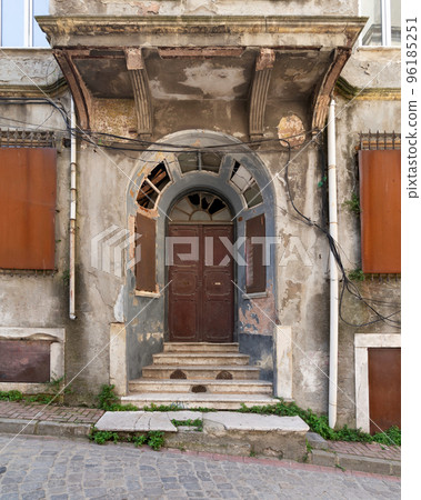 Grungy abandoned entrance with rusted metal door, and stairs, on a cobblestone narrow street  96185251