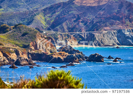 View of Bixby Bridge on west coast from distance surrounded by mountains 97197586