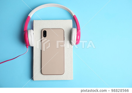 Book, modern headphones and smartphone on light blue background, top view. Space for text 98828566