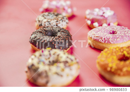 Doughnuts with multicolored glaze laid out in two rows on trendy pink background. Doughnuts are traditional sweet pastries. Copy space for text. 98980833