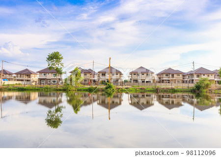 New house building reflection with water in lake at residential estate construction site with clouds and blue sky 98112096