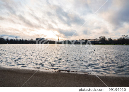 Scenic view of beautiful lake with silhouette St Mary Abbots church and Kensington Palace in the background. Cloudy day during sunset in London 99194930