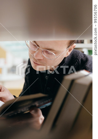 confident man chooses books on shelf in library, education at university or independently online, 99356706