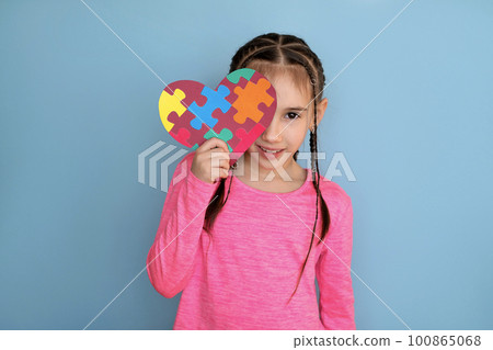 A beautiful stylish girl gently holds a heart-shaped card with puzzles, covering part of her face. The unity of humanity in relation to special people, unlike others 100865068