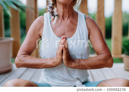 A senior woman sitting outdoors on a terrace in summer, doing yoga exercise,close-up. 100988236