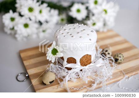 Easter cake in glaze with a ribbon stands on a board with quail eggs and white flowers 100990830