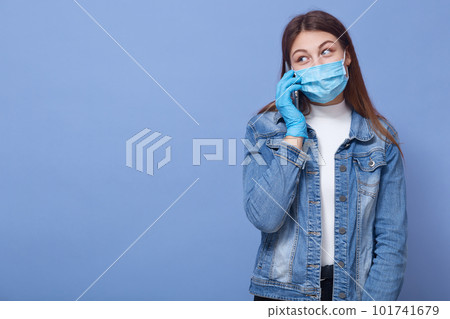 Image of darkhaired female wearing casual outfit, disposable medical flumask and protective gloves, taking to her friend about sutiation in country regarding to coronavirus. Covid 19 concept. 101741679