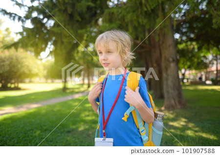 Elementary student boy with backpack, bottle of water and name badge on his neck goes to school. Happy child is waiting of school bus. 101907588