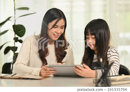 Cute schoolgirl doing homework or learning online with mother at home. Homeschooling, learning and family concept 101335704