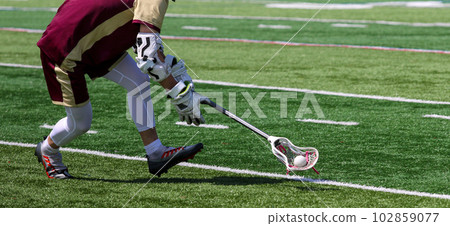 Lacrosse player running and scooping up the ball during a game 102859077