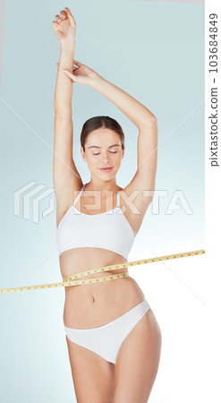 I look good because I worked for it. Studio shot of a young woman measuring her waist against a blue background. 103684849