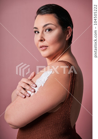 Body positive woman applying moisturising cream on her shoulder 104505222