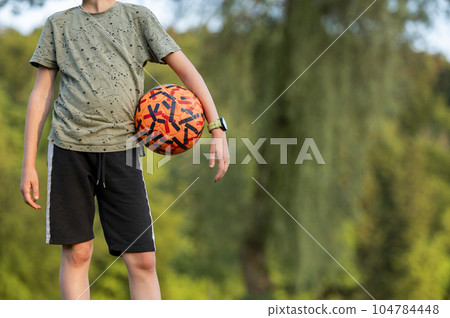 Teenage boy in a soccer practice standing with an orange ball under his arm 104784448