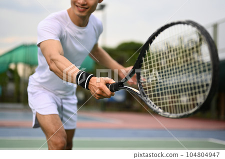 Smiling muscular man hitting ball with racket to return ball over net. Sport, fitness, training and active life concept 104804947