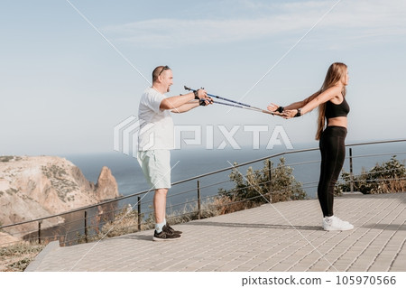 Happy Middle aged couple or friends practicing nordic walking in park near sea. Mature couple with trekking poles walking, practicing Nordic walking outdoors. Aging youthfully and sport concept 105970566