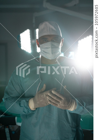 Portrait of biracial male surgeon wearing surgical gown in operating theatre at hospital 105972685