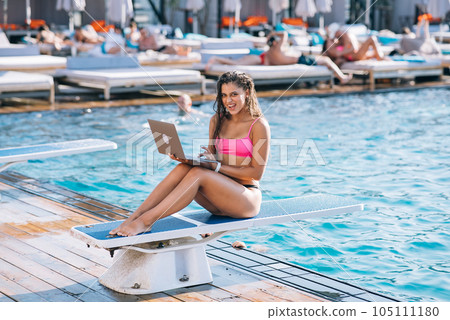 Cute young woman in swimsuit sunbathing with a laptop in a pool 105111180