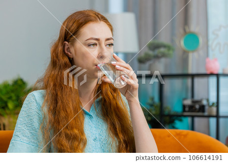 Thirsty young woman sitting at home holding glass of natural aqua make sips drinking still water 106614191