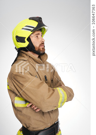 Strong, serious guy in fireman's uniform looking up and away in studio. Side view of firefighter waiting, with crossed hands, isolated on white background. Concept of work, firefighting, hope. 106647363