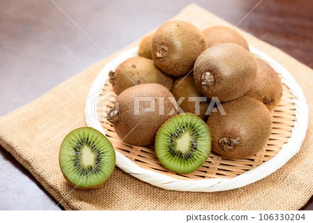 Kiwi fruit piled high in a colander on top of a jute bag and kiwi sliced into rings with visible cross-sections 106330204