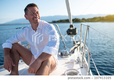 Man in white clothes sitting on a yacht deck and looking relaxed and happy 107413105