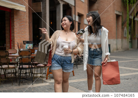 Two cheerful young Asian women friends are enjoying talking during their shopping day in the city. 107484165