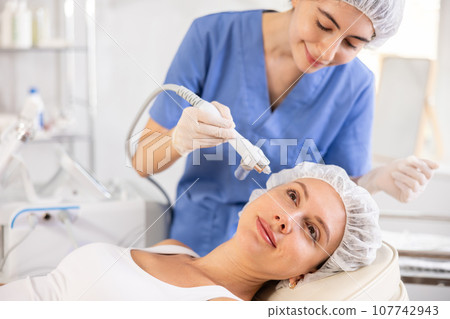 Female patient undergoing facial skin ionization procedure using ion airbrush 107742943