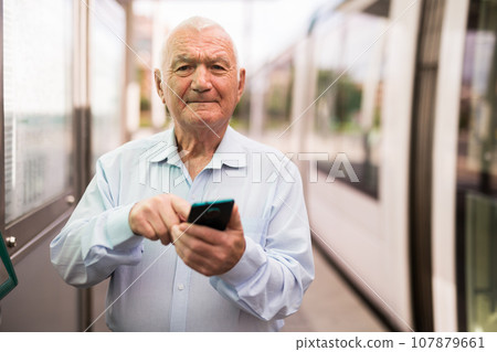 Senior man using smartphone while standing on tram stop 107879661