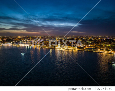 Amazing evening shot of illuminated streets and buildings in city. Boats on water surface around. Night life in metropolis. Istanbul, Turkey 107251950