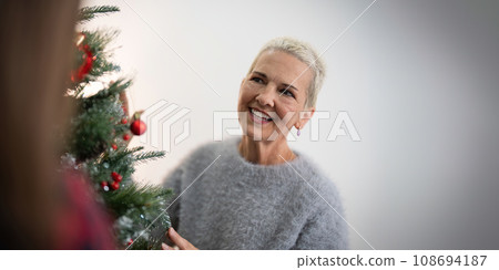 Cheerful elderly woman decorat the christmas tree. Christmas atmosphere at cozy home interior 108694187